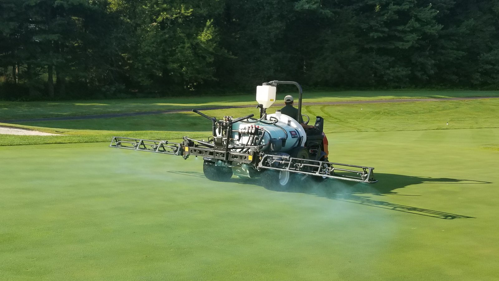 Sprayer boom applying mist over maintained turf